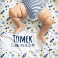 Biały kocyk z imieniem dziecka i nadrukiem w rakiety kosmiczne i planety. Grafiki mają kolory niebieski i żółty. Biała chmurka z imieniem malucha.