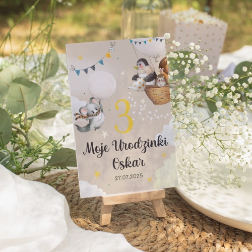 Tabliczka rezerwacyjna na stolik z personalizowanym napisem z imieniem dziecka. Tabliczka stoi na drewnianej mini sztaludze