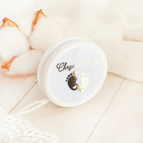 Jojo prezent dla gości na Chrzest Święty. Na białej zabawce jest okrągła etykieta z uniwersalną treścią. Złoty rysunek dziecięcych stópek dopełniliśmy napisem. Pomysłowy upominek dla bliskich.