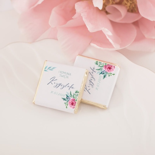 Belgijska czekolada zapakowana złote opakowanie, na którym znajduje się biała etykieta z grafiką fuksjowy jaskier z imieniem oraz data uroczystości.