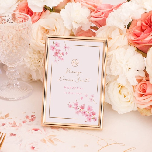 Tabliczka na stolik komunijny w złotej ramce. Białą kartkę zdobią różowe kwiaty magnolii, napis "Pierwsza Komunia Święta", którego dopełnia wybrana przez Was personalizacja.