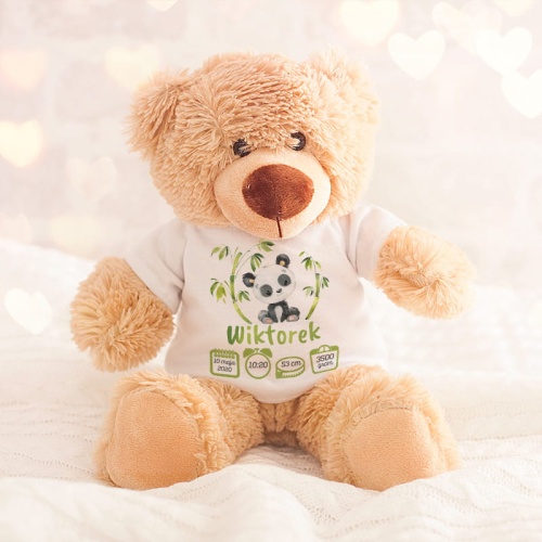 Beżowy, pluszowy miś w białej koszulce na krótki rękaw. Na jej przodzie jest rysunek małej pandy, siedzącej pomiędzy pędami bambusa. Pod spodem jest imię dziecka oraz informacje z metryki urodzenia.