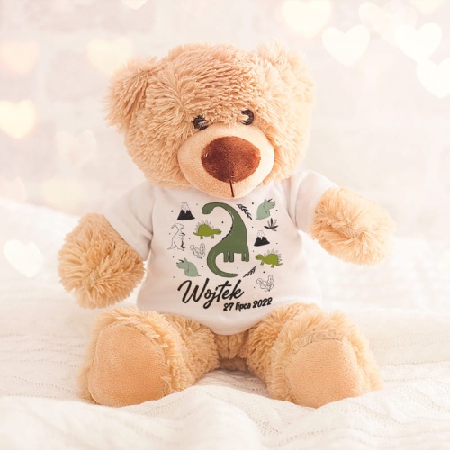 Pluszowy miś w beżowym kolorze z białą koszulką na krótki rękaw. Na tshircie kolorowa grafika dinozaurów, imię dziecka oraz data urodzenia.