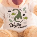 Miś pluszowy dla dziecka na narodziny. Pluszanka ma białą koszulkę z ilustracją dinozaurów, imieniem dziecka i datą narodzin.