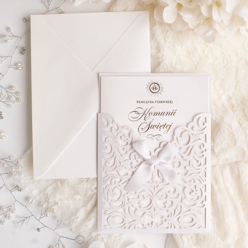 Kartka na pamiątkę I Komunii z ażurowymi detalami i białą kokardką na froncie.