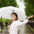 Parasolka komunijna, w kolorze białym, automatyczna. Na zdjęciu dziewczynka trzymająca parasolkę na tle zielonych drzew w parku.